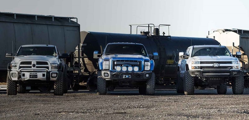 three different brands of diesel trucks lines up in front of a train